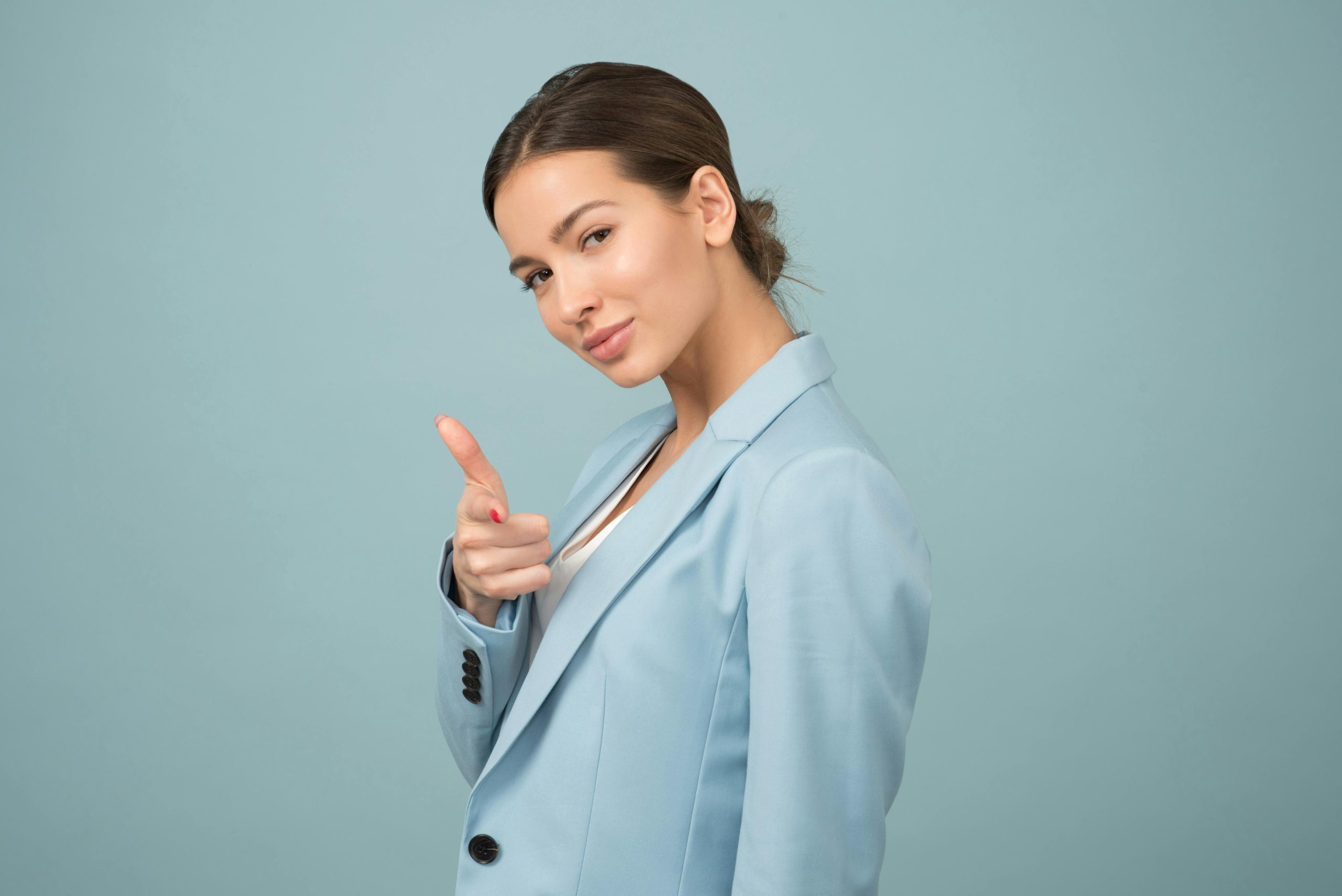 Home A young woman in a blue suit exhibits confidence with a relaxed pose against a blue background.